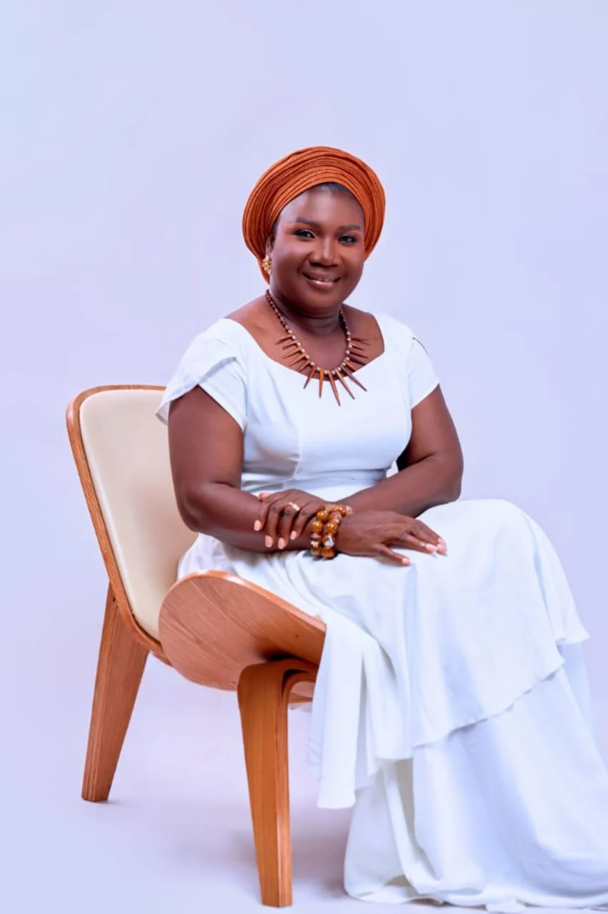Sika Coleman seated in a white dress with an orange headwrap